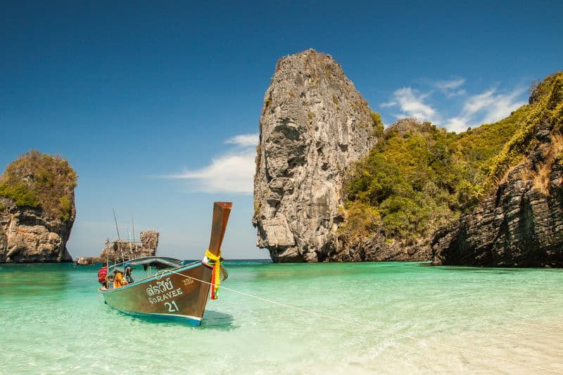 A longtail boat in turquoise water beside limestone cliffs, Thailand