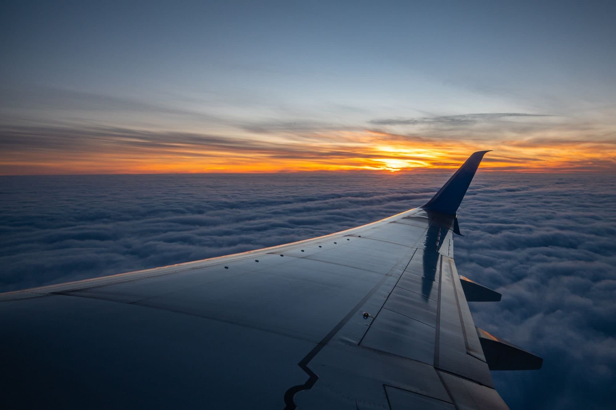 An aircraft wing above a sea of cloud at sunset